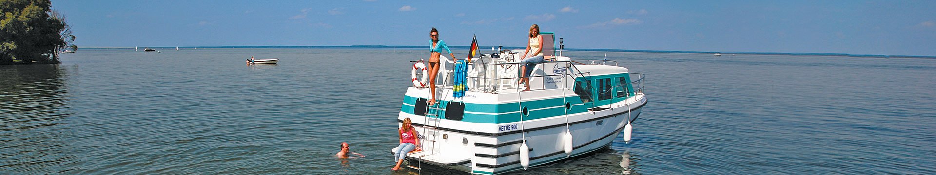 Ein Hausboot ankert auf der Müritz. Die Urlauber baden im Wasser oder genießen die Sonne.