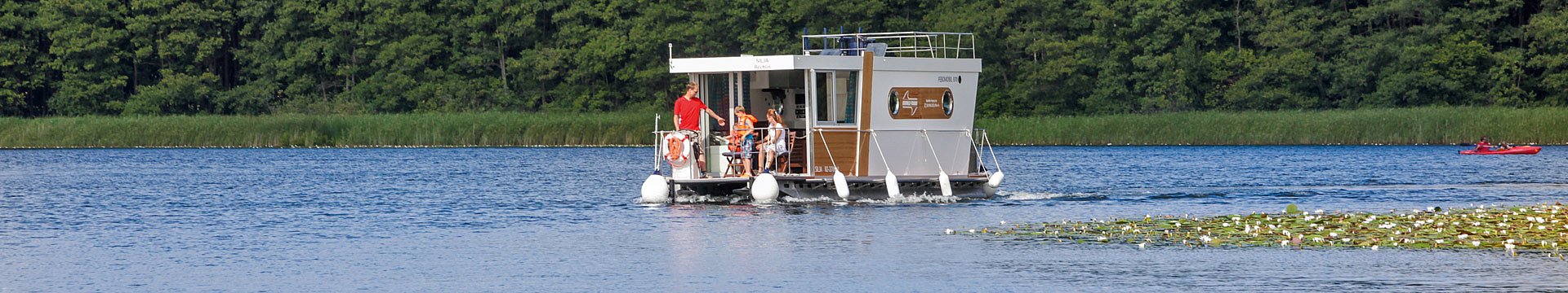 Das Hausboot Febomobil fährt mit einer Familie über einen See.