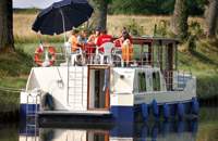 ein Hausboot hat an einem Flussufer in Frankreich angehalten. Ein Sonnenschirm schützt vor zu viel Sonne.