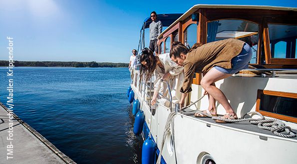 Das Boot des Typen Kormoran fährt auf einen Steg zu und zwei Frauen werfen die Seile aus, um anzulegen.
